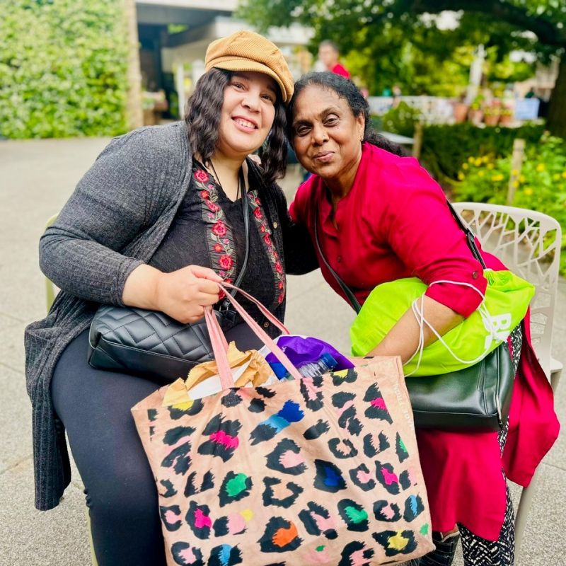 two carers sitting next to each other smiling on a social trip to Kew Gardens